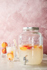 Peach cocktail in glass and jar with tap on table. Refreshing drink