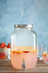 Peach cocktail in jar with tap on table. Refreshing drink