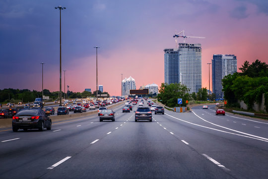 Night traffic. Cars on highway road at sunset evening in typical busy american city. Beautiful amazing night urban view with red, yellow and blue sky clouds. Sundown in downtown.
