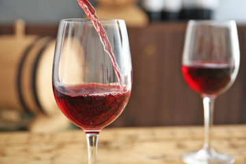 Pouring delicious red wine into glass on table, closeup