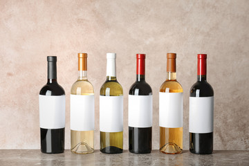 Bottles with different wine on table against color background
