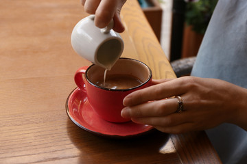 Woman adding milk to fresh aromatic coffee at table, closeup