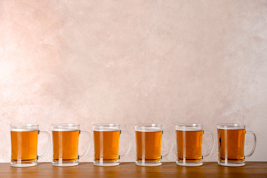 Glass mugs with beer on table against color background
