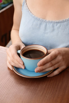 Woman with cup of fresh aromatic coffee at table, closeup