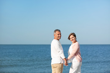 Fototapeta na wymiar Happy mature couple holding hands at beach on sunny day