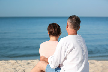 Happy mature couple sitting together at beach on sunny day