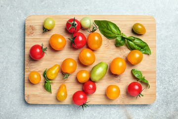 Wooden board with juicy tomatoes on grey background, top view