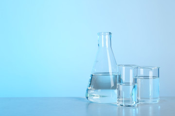 Laboratory glassware with liquid on table against color background. Chemical analysis