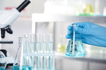 Analyst holding flask with fluid in laboratory, closeup. Chemical analysis