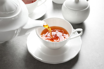 Pouring hot tea into porcelain cup on table