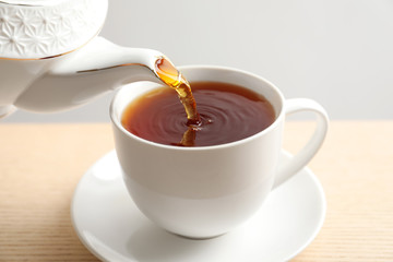 Pouring hot tea into porcelain cup on wooden table