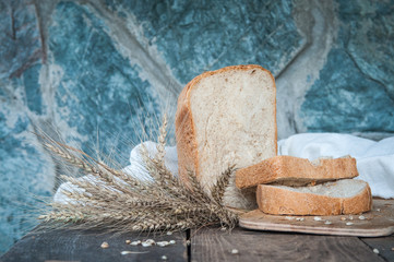 Fresh, homemade bread. Composition on a wooden background with cut pieces of bread, ears and grains. Soft blurred background.
