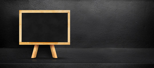 Blank blackboard leaning at black interior cement room background,banner mock up template for display of design,leave side space for adding text for advertising.