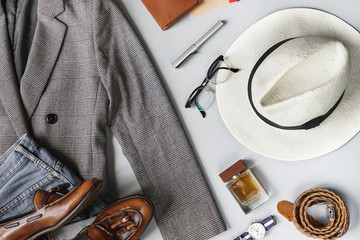 Top view set of classic clothes, plaid blazer, brown tassel loafer, brimmed straw hat and accessories on grey background