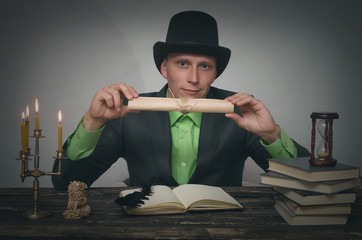 Man in bowler hat and suit is sitting by table and showing in hands a document scroll. Writer,...