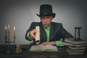 Man in bowler hat and suit is sitting by table and showing in hands a document scroll. Writer,...