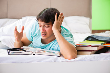 Student preparing for exams at home in bedroom lying on the bed