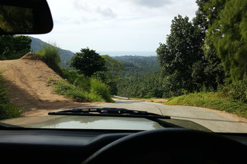 Fototapeta na wymiar Road through jungle, view behind windshield of car. Koh Samui, Thailand. Concept: trip, exotic place