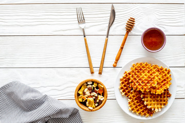 Traditional belgian waffles near dried fruit, nuts and honey on served table with tablecloth on white wooden background top view copy space