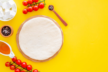 Ingredients for cooking vegetarian pizza. Rolled pizza dough, cherry tomatoes, olive oil, cheese mozzarella, spices on yellow background top view mockup copy space