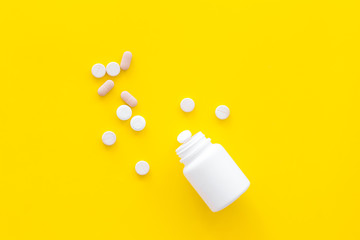 Medicine. Pills falling out of jar on yellow background top view copy space