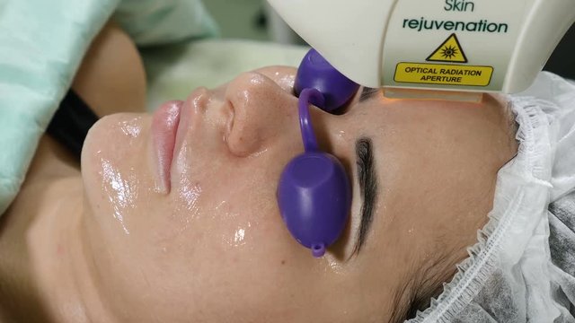 Skin care. Woman with glasses on eyes getting photo rejuvenation procedure in a beauty salon. Beautician performing facial procedure. Shot in 4k