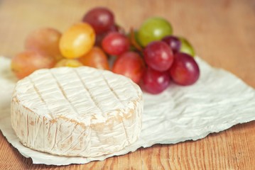 A soft ripened Camembert cheese and grapes on a wooden board