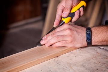 Close up of a young  man builder  treating a wooden product with a chisel in the workshop