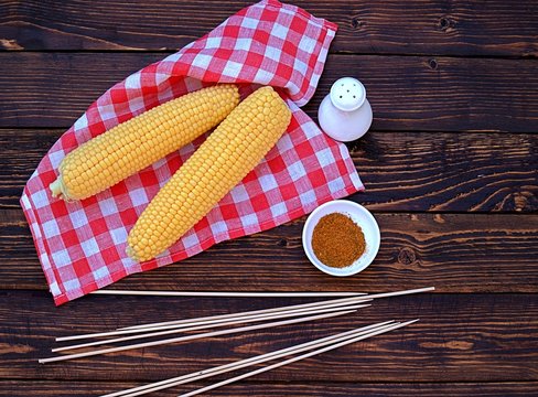 Ingredients for cooking corn grill on a wooden background. Fresh organic corn cobs, wooden skewers, spices, salt. Top view