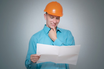 Happy builder construction worker is holding in hand a plan draft document isolated on gray background.