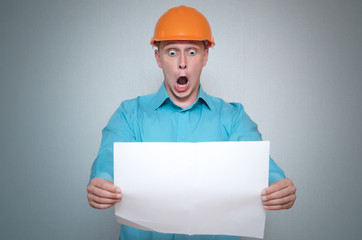 Shocked builder construction worker is holding in hand a plan draft document isolated on gray...