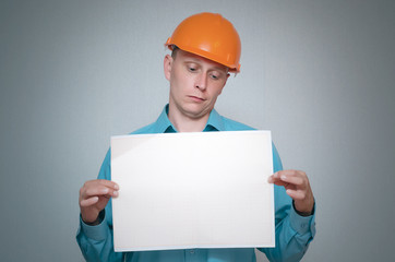 Serious builder construction worker is holding in hand a plan draft document isolated on gray background.