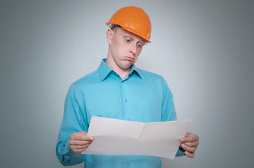 Perplexed builder construction worker is holding in hand a plan draft document isolated on gray background.