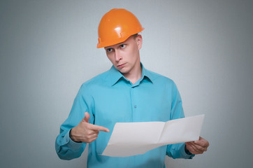 Confused builder construction worker is holding in hand a plan draft document isolated on gray background.