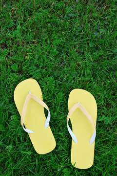 Yellow flip flops on green field background top view image with copy space for text on grass. Summertime leisure concept.