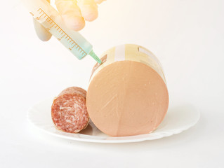Sausage on a white background in which a syringe is injected with antibiotic and preservatives, close-up, snag hormone