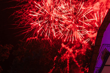 Explosions of red fireworks on the background on a dark night sky and hotel balcony