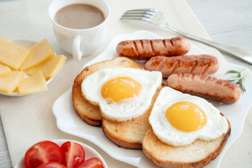 Breakfast with love - fried eggs in the shape of a heart, fried sausages and coffee
