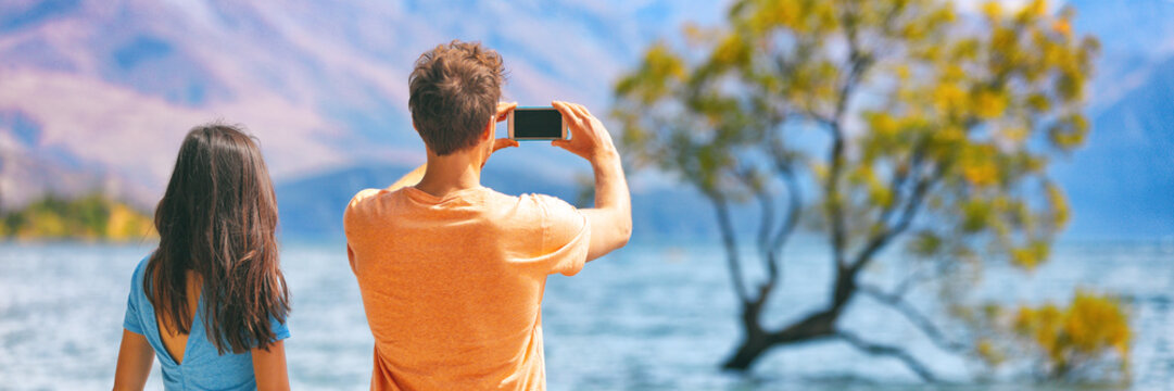 Travel lifestyle people tourists taking picture with phone on New Zealand Wanaka tree background Vacation couple banner panorama.