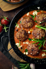 Meatballs in tomato sauce in a cast iron skillet on a wooden rustic board on a dark background