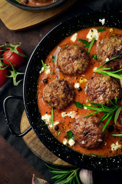 Meatballs in tomato sauce in a cast iron skillet on a wooden rustic board on a dark background