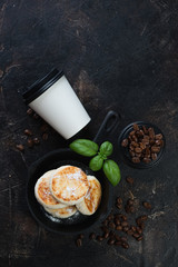 Cast-iron frying pan with cottage cheese pancakes and coffee, flatlay over dark brown stone background with copy space