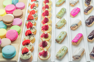 Pastry shop display window with variety of eclairs, macarons, tarts, selective focus