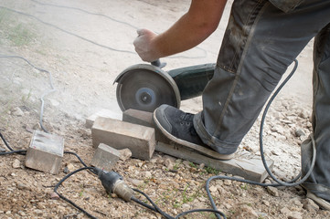 Worker with electrical saw cutting pavement tiles in smaller pieces