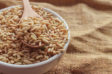 Raw brown rice in a spoon and bowl. top view food background