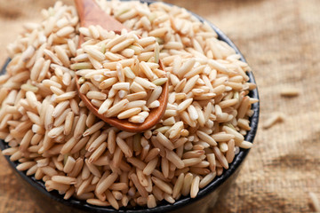 Raw brown rice in a spoon and bowl. top view food background