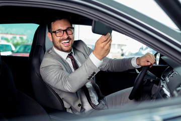 Handsome businessman is sitting in a new car in car dealership