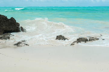 Blue waves break on the coastal rocks. Salt water spray in the light of the sun. Beach on Zanzibar island, Tanzania