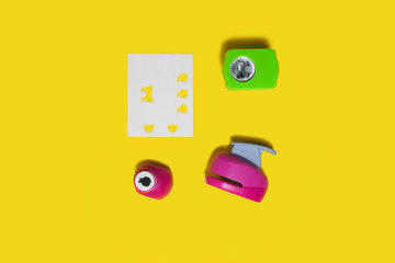 three small colored plastic hole punchers near sheet of paper standing on the yellow background....