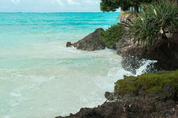 Blue waves break on the coastal rocks. Salt water spray in the light of the sun. Beach on Zanzibar...
